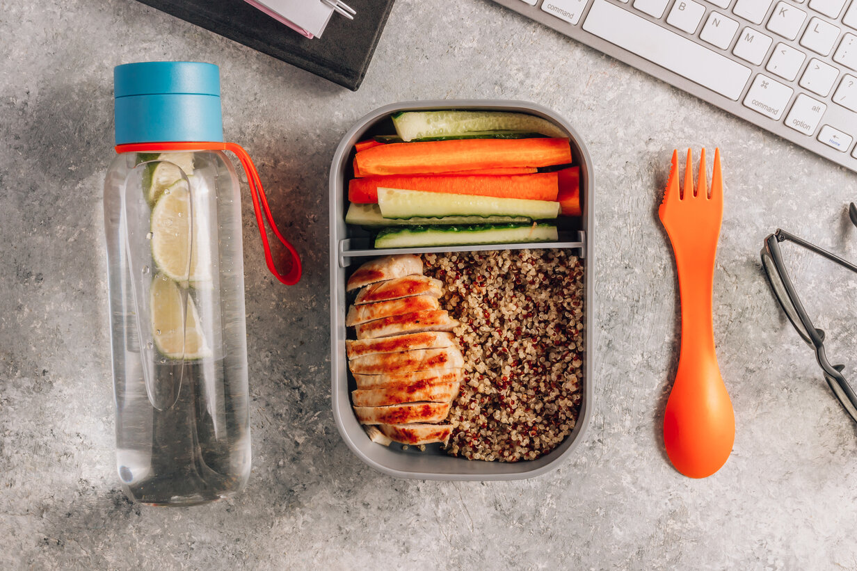 Healthy meal prep containers with quinoa, chicken and and sticks of cucumber and carrots on light gray background. Healthy lunch at work. Take away concept.