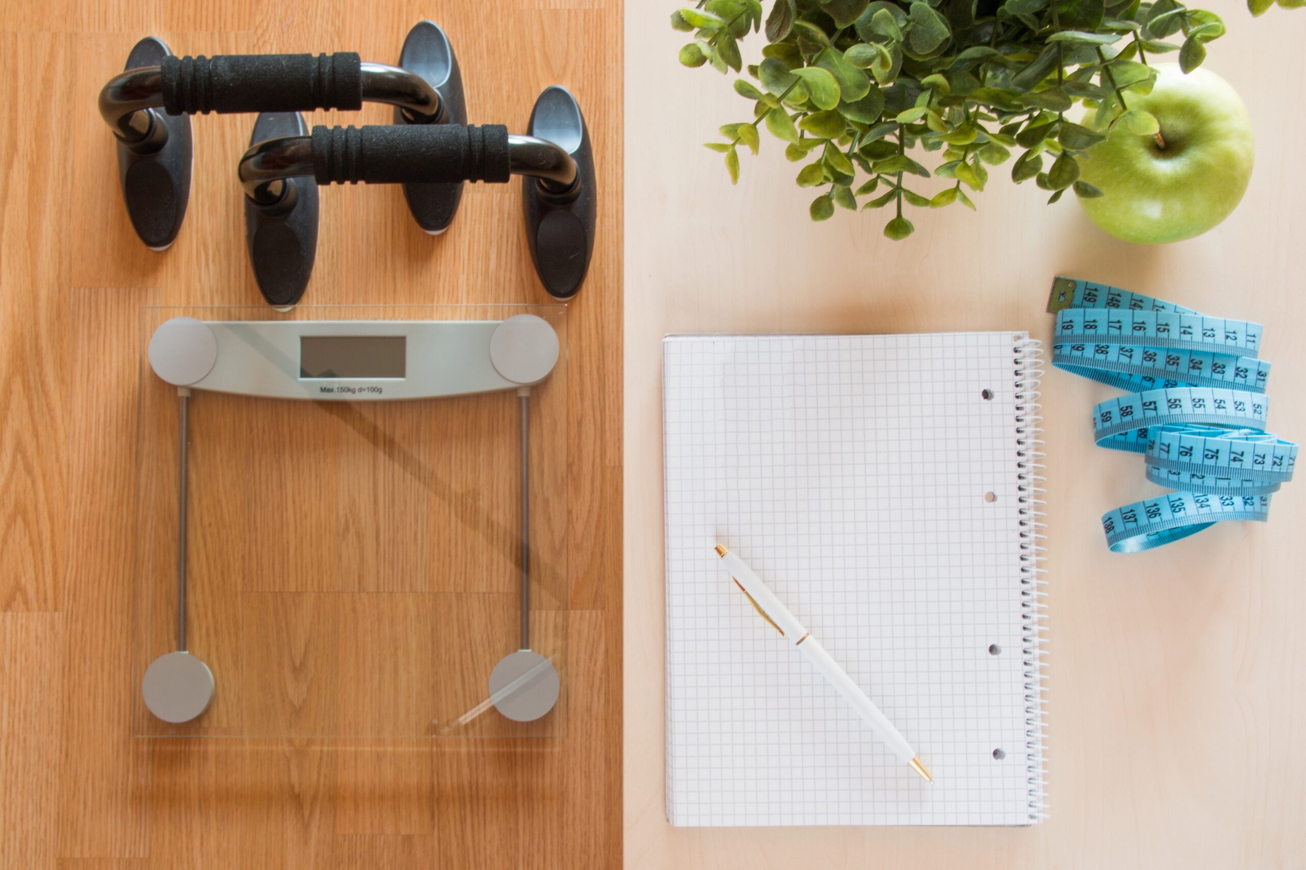 Fitness and weight loss concept, scale and notebook on a wooden table, top view
